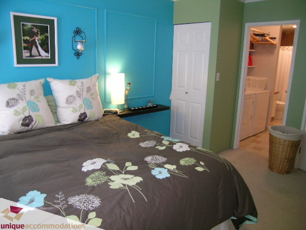 Furnished bedroom with floral bedding, teal walls, and closet access. - 50 - 900 West 17th, North Vancouver