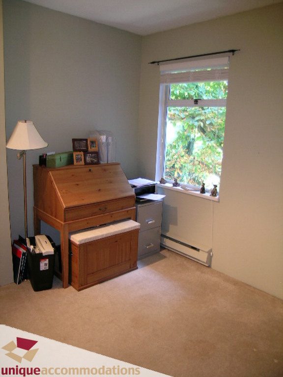 Den with wooden desk, lamp, and window view of greenery. - 50 - 900 West 17th, North Vancouver