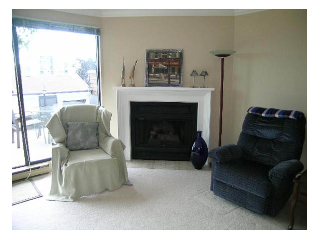 Living room with fireplace, large window, and cozy seating. - 3-220 East 4th Street, North Vancouver