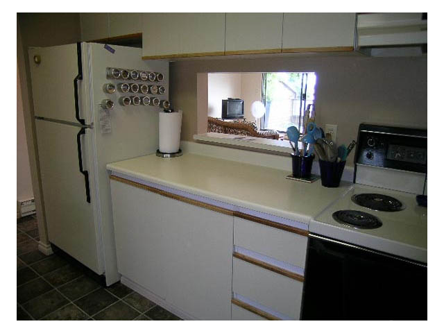 Bright kitchen with white countertops and a window view, featuring a refrigerator and a stove. - 3-220 East 4th Street, North Vancouver