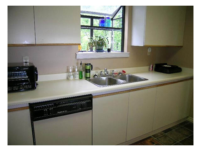 Bright kitchen with white cabinets, black appliances, and a window with a view of greenery. - 3-220 East 4th Street, North Vancouver