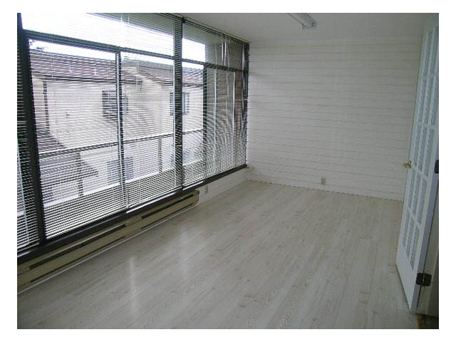 Bright living room with hardwood floors and large windows, showcasing a city view. - 3-220 East 4th Street, North Vancouver