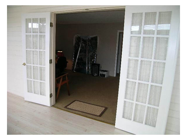 Bright living room with French doors leading to a cozy bedroom, hardwood floors, and a small rug. - 3-220 East 4th Street, North Vancouver
