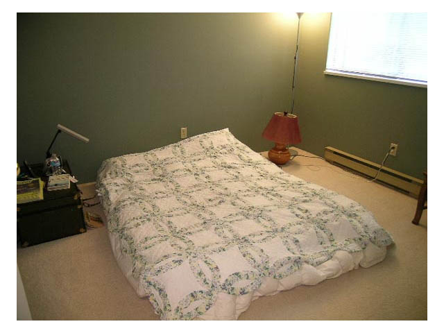 Bedroom with neatly made bed, green walls, and bedside lamp. - 3-220 East 4th Street, North Vancouver