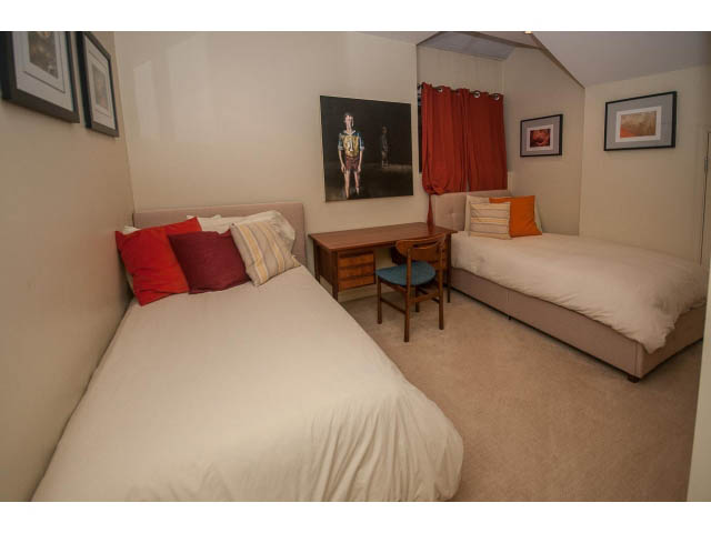 Furnished bedroom with two single beds, red and orange pillows, and a small table. - 1882 Whyte Avenue, Vancouver West Side
