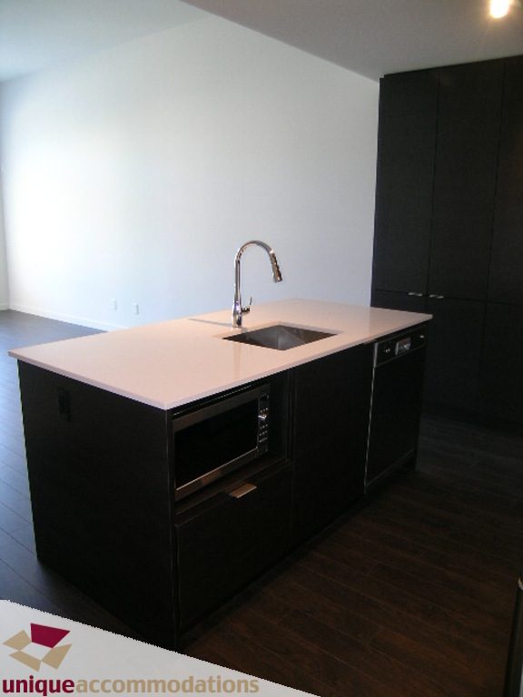 Bright kitchen with dark cabinetry, white countertops, and hardwood floors. - 510 - 1677 Lloyd Avenue, North Vancouver