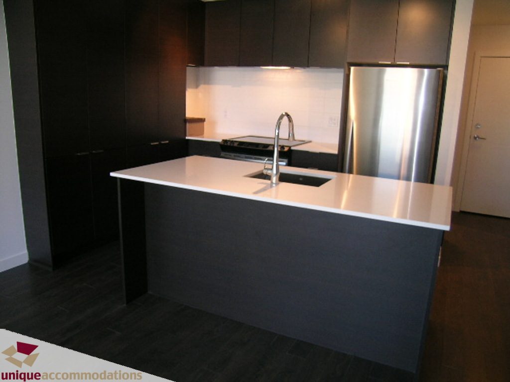 Bright kitchen with modern island, white countertops, dark cabinets, and stainless steel appliances. - 510 - 1677 Lloyd Avenue, North Vancouver