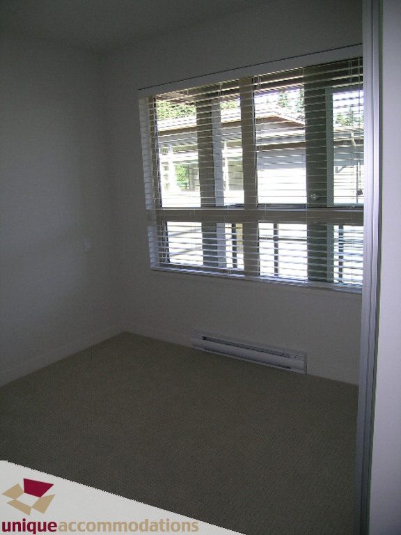 Bright living room with large window, blinds, and carpeted floor. - 510 - 1677 Lloyd Avenue, North Vancouver