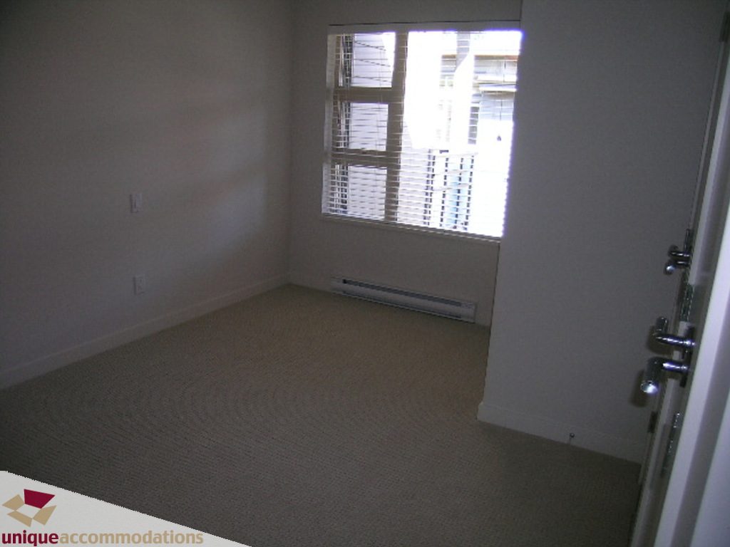 Bright bedroom with beige carpet and large window with blinds. - 510 - 1677 Lloyd Avenue, North Vancouver