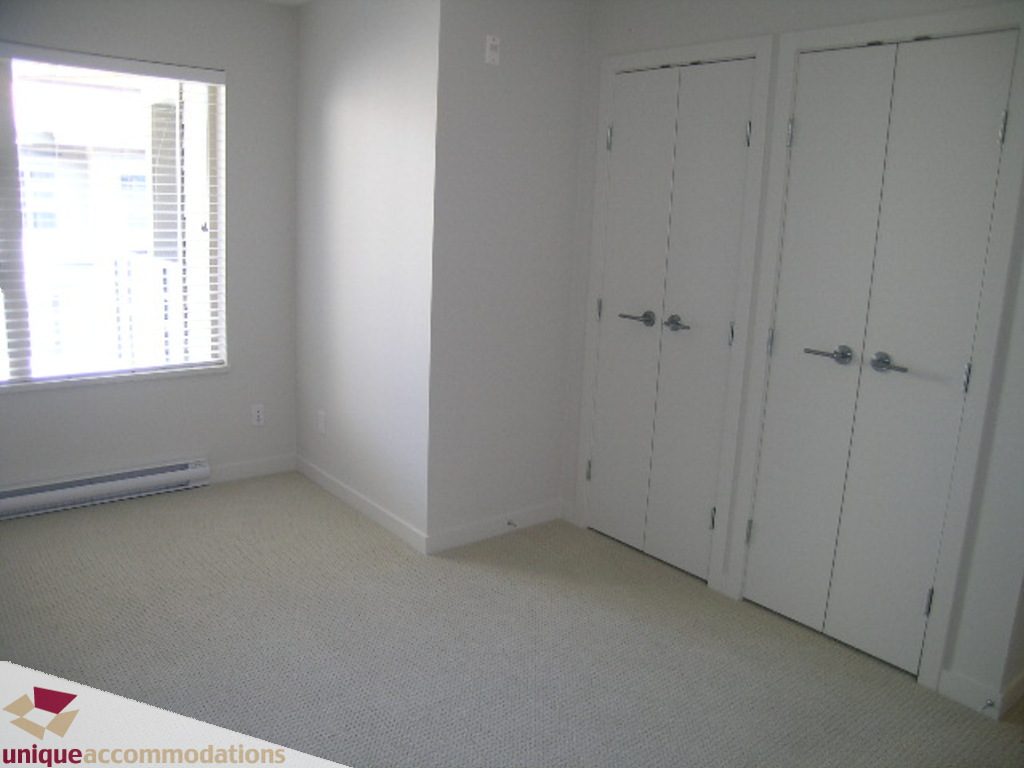 Bright bedroom with white walls, carpeted floor, and large window with blinds. - 510 - 1677 Lloyd Avenue, North Vancouver