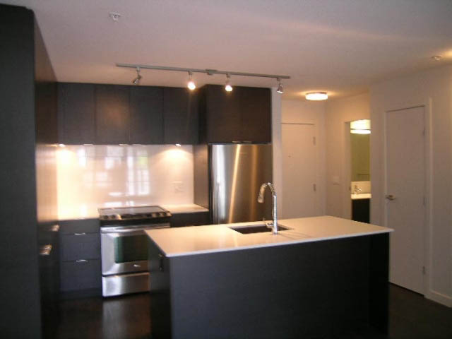 Bright kitchen with modern black cabinetry and stainless steel appliances, featuring a dark countertop and hardwood floors.