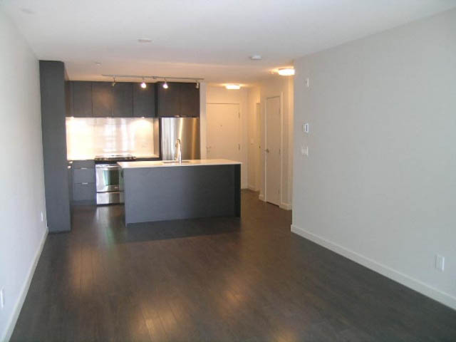 Open-concept living space with dark countertops and hardwood floors. - 302 - 1677 Lloyd Avenue, North Vancouver