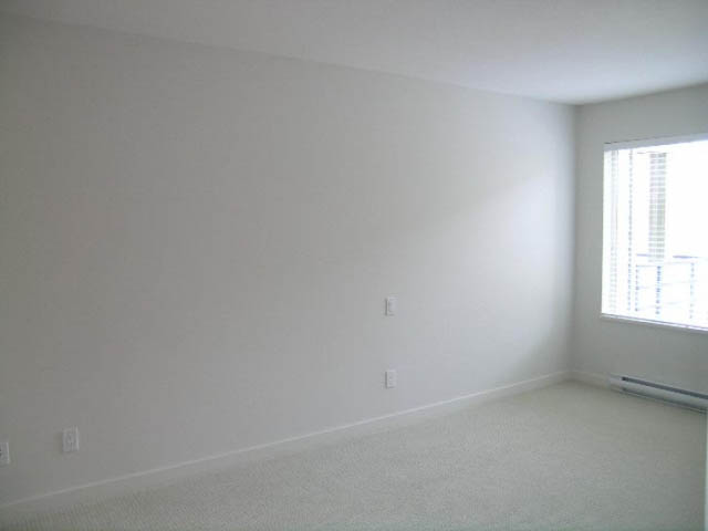 Bright living room with carpeted floor and large window. - 302 - 1677 Lloyd Avenue, North Vancouver