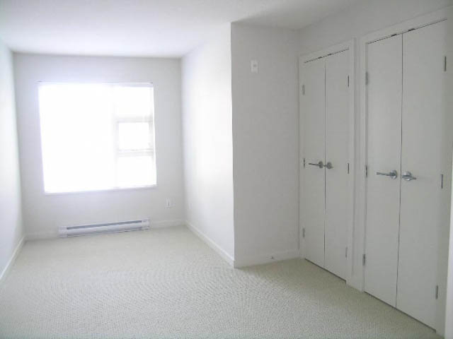 Bright bedroom with white walls, built-in cabinets, and a large window. - 302 - 1677 Lloyd Avenue, North Vancouver
