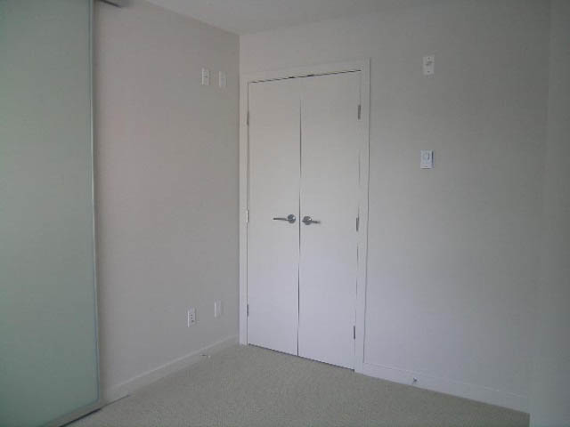 Bright bedroom with white walls and a closed door. - 302 - 1677 Lloyd Avenue, North Vancouver