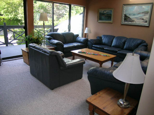 Furnished living room with leather couches, coffee table, and large sliding glass doors leading to a patio. - 1077 Blue Grouse Way, North Vancouver