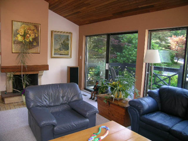 Spacious living room with leather furniture, large windows, and a view of greenery. - 1077 Blue Grouse Way, North Vancouver