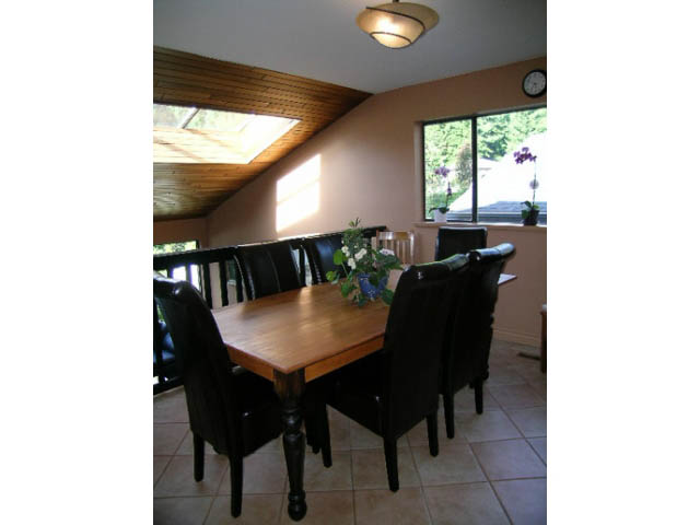 Bright dining area with wooden table and chairs, natural light from large window, and a slanted ceiling. - 1077 Blue Grouse Way, North Vancouver
