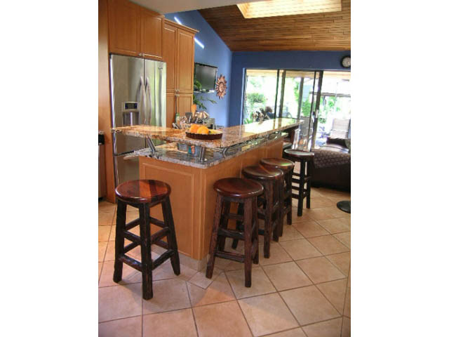 Bright kitchen with granite countertops and wooden bar stools, leading to a sunlit dining area. - 1077 Blue Grouse Way, North Vancouver