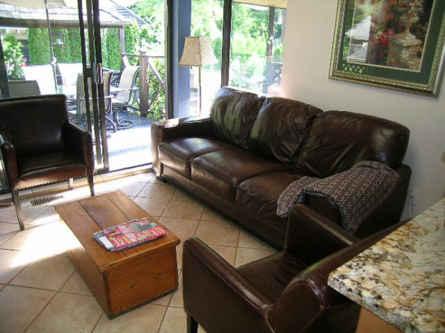 Living room with leather furniture, granite countertops, and large windows showing greenery. - 1077 Blue Grouse Way, North Vancouver