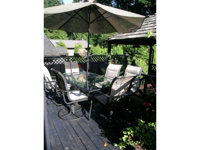 Furnished patio with outdoor furniture and umbrella, surrounded by greenery. - 1077 Blue Grouse Way, North Vancouver