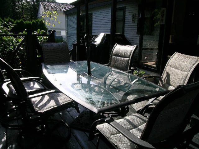 Furnished patio with glass table and wicker chairs, surrounded by greenery. - 1077 Blue Grouse Way, North Vancouver