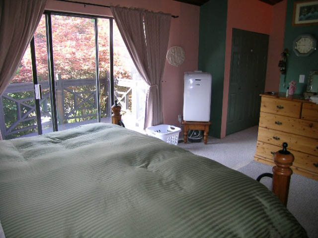 Furnished bedroom with green bedding, wooden dresser, and sliding glass door to balcony. - 1077 Blue Grouse Way, North Vancouver