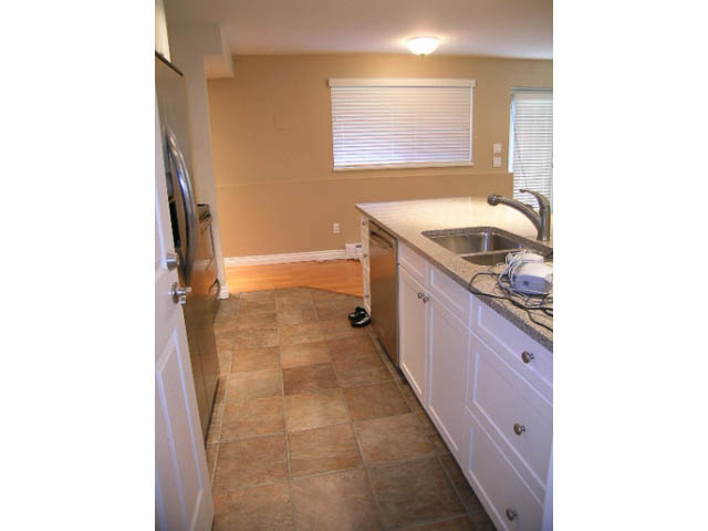 Bright kitchen with white cabinets, granite countertops, and tiled flooring. - 1077 Blue Grouse Way, North Vancouver