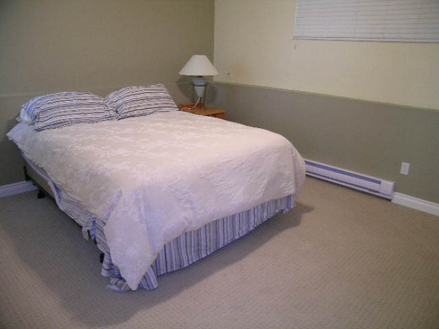 Bright bedroom with neatly made bed, striped bedding, and simple decor. - 1077 Blue Grouse Way, North Vancouver