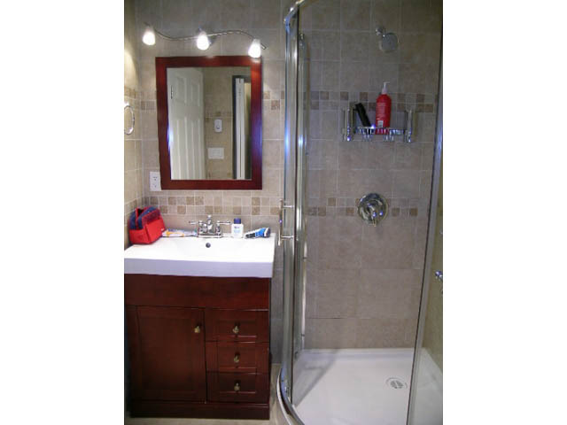 Bathroom with wooden vanity, glass shower, and beige tile walls. - 1077 Blue Grouse Way, North Vancouver
