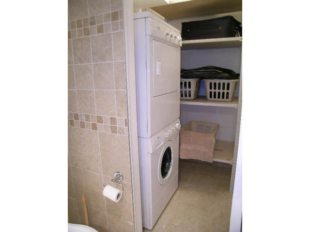 Bright laundry room with stacked washer and dryer, tiled walls, and storage shelves. - 1077 Blue Grouse Way, North Vancouver