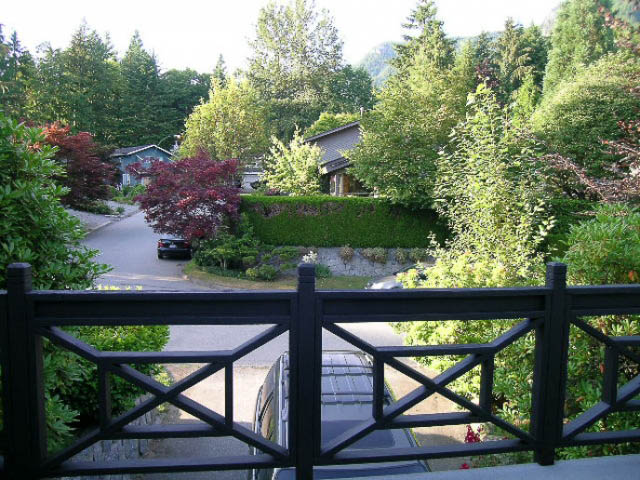 Balcony view of lush greenery and a quiet street, framed by a black railing. - 1077 Blue Grouse Way, North Vancouver