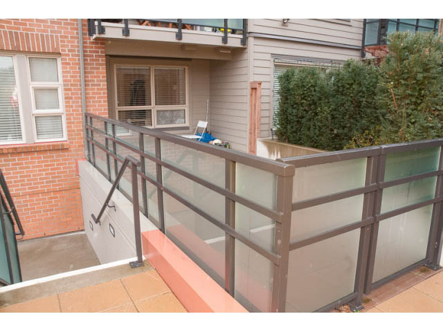 Furnished balcony with glass railings and brick wall. - 215 - 1677 Lloyd Avenue, North Vancouver