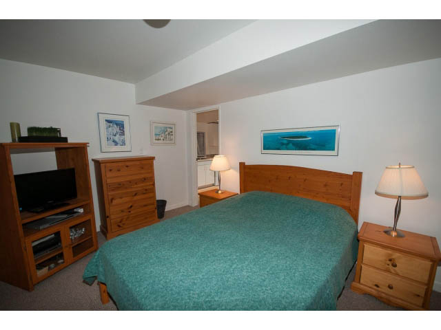 Furnished bedroom with wooden furniture, teal bedding, and a nightstand lamp. - Cottage - 1395  3rd Street, West Vancouver