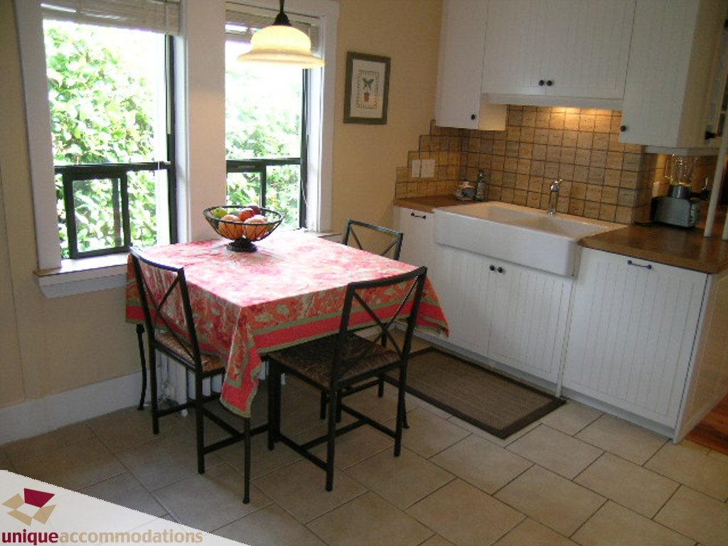 Bright kitchen with white cabinets, tiled backsplash, and a dining table with red tablecloth. - 813 - 5th Street East, North Vancouver