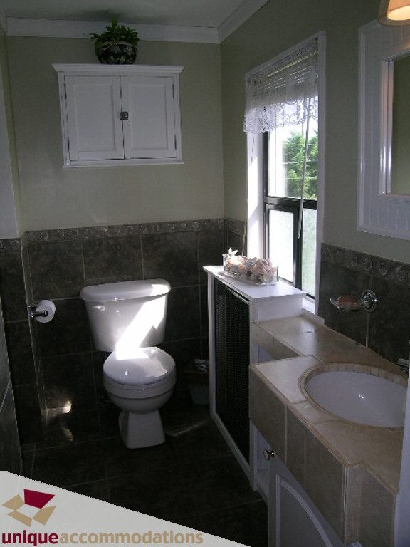 Bright bathroom with dark tiled walls, white countertop, and natural light from window. - 813 - 5th Street East, North Vancouver