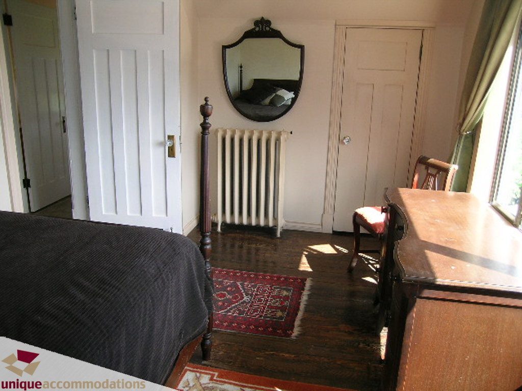 Furnished bedroom with wooden floors, antique mirror, and radiator. - 813 - 5th Street East, North Vancouver