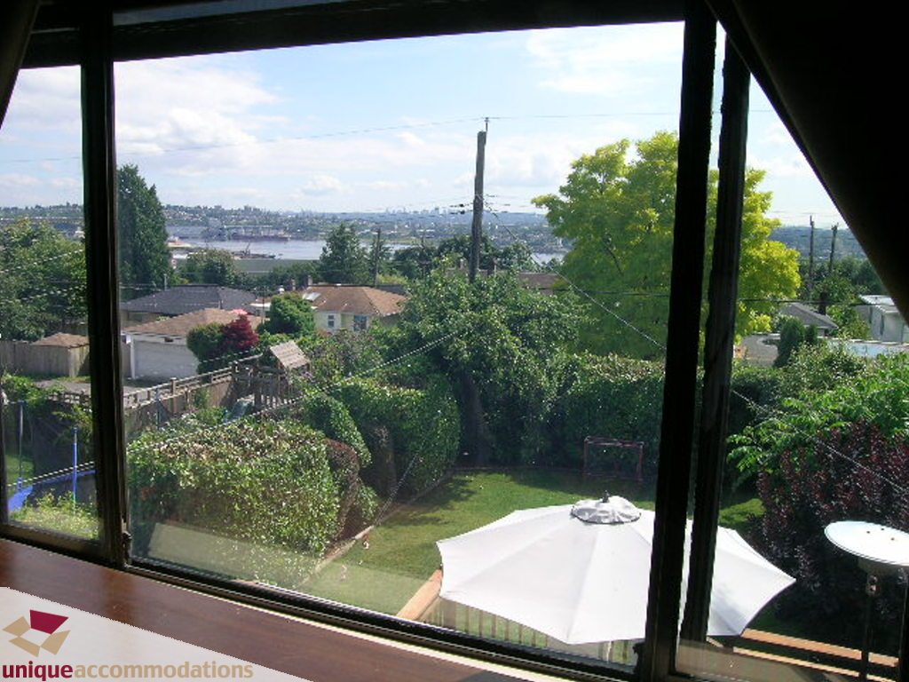 Bright living room with city view and lush greenery, hardwood floors and patio furniture. - 813 - 5th Street East, North Vancouver