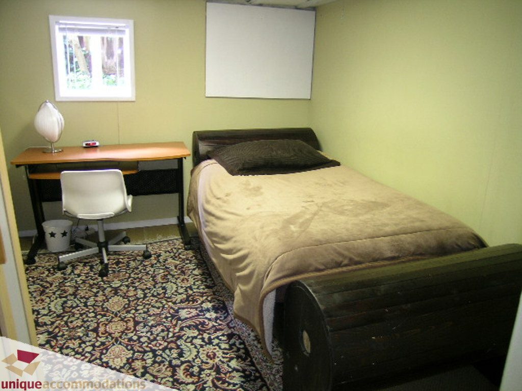 Furnished bedroom with wooden bed, desk, and patterned rug. - 813 - 5th Street East, North Vancouver