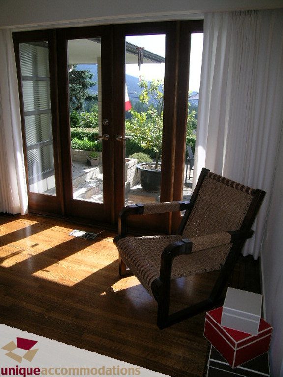 Bright sunlit living room with hardwood floors, large windows, and a comfortable armchair. - 68 Bonnymuir Drive, West Vancouver