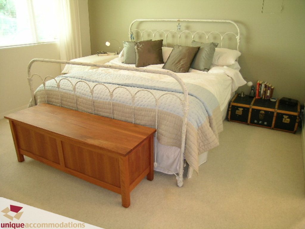 Bright bedroom with white metal bed frame, wooden storage bench, and neatly arranged pillows. - 68 Bonnymuir Drive, West Vancouver