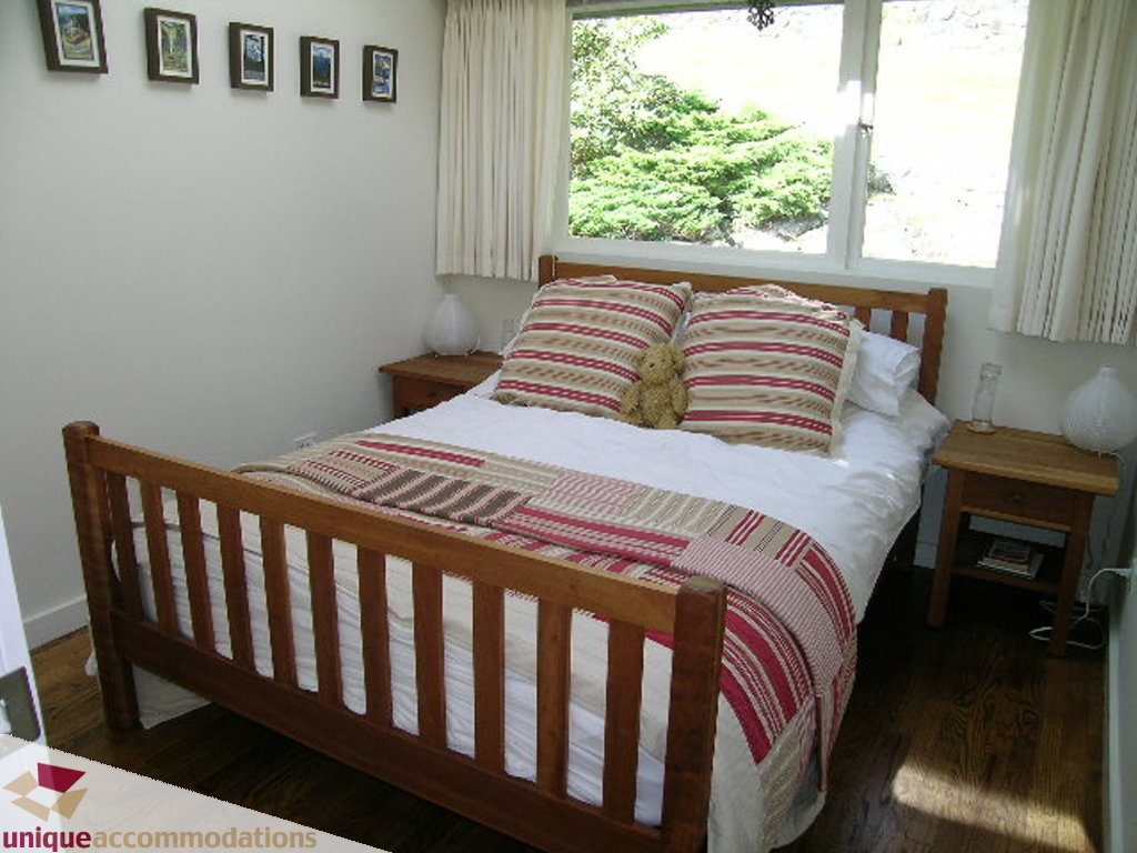 Bright bedroom with wooden bed, striped bedding, and natural light from window. - 68 Bonnymuir Drive, West Vancouver