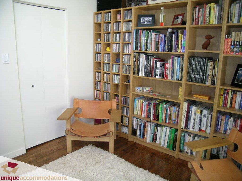 Bright living room with wooden floors, large bookshelf, and comfortable armchair. - 68 Bonnymuir Drive, West Vancouver