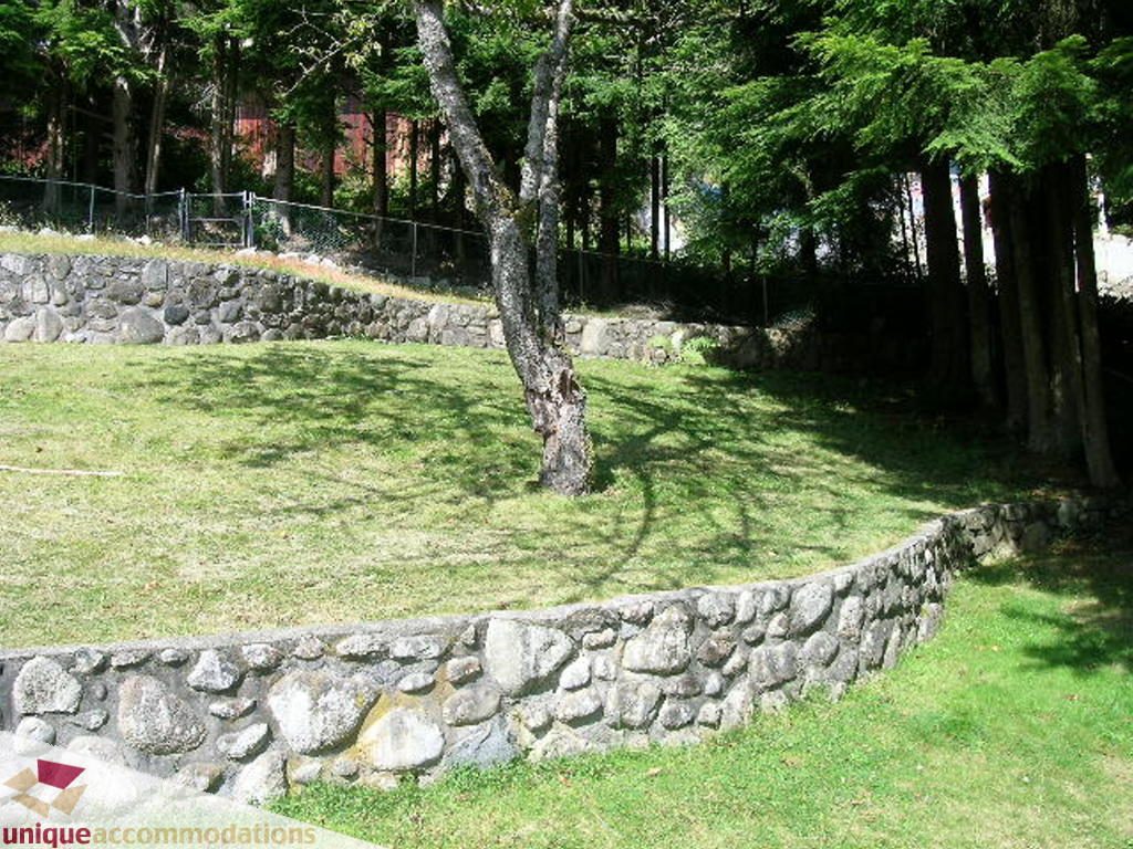 Fenced grassy yard with stone wall and tree. - 68 Bonnymuir Drive, West Vancouver