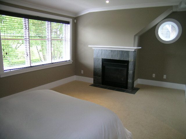 Furnished bedroom with a large window, beige walls, and a stone fireplace. - 3670 Point Grey Road, Vancouver West Side