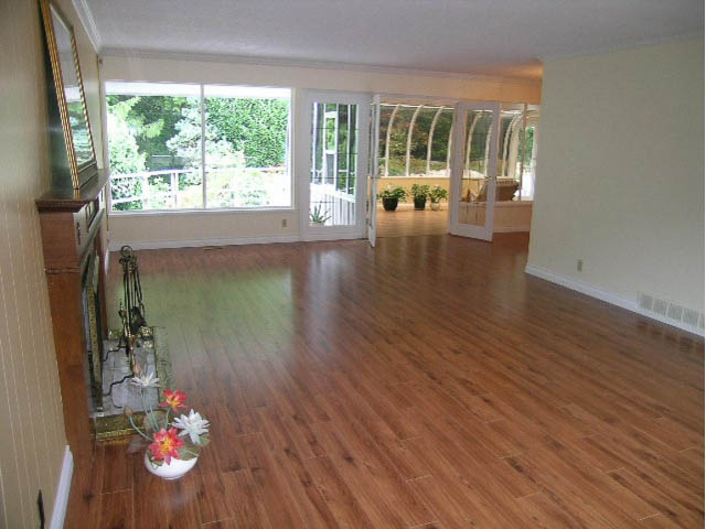 Bright living room with hardwood floors and large windows, leading to a patio with greenery. - 5725 Cranley Drive, West Vancouver