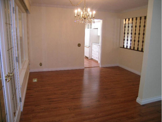 Bright dining area with hardwood floors and chandelier, leading to a kitchen with white cabinets. - 5725 Cranley Drive, West Vancouver