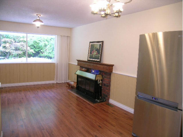 Bright living room with hardwood floors and a fireplace, featuring a chandelier and a large window with a city view.