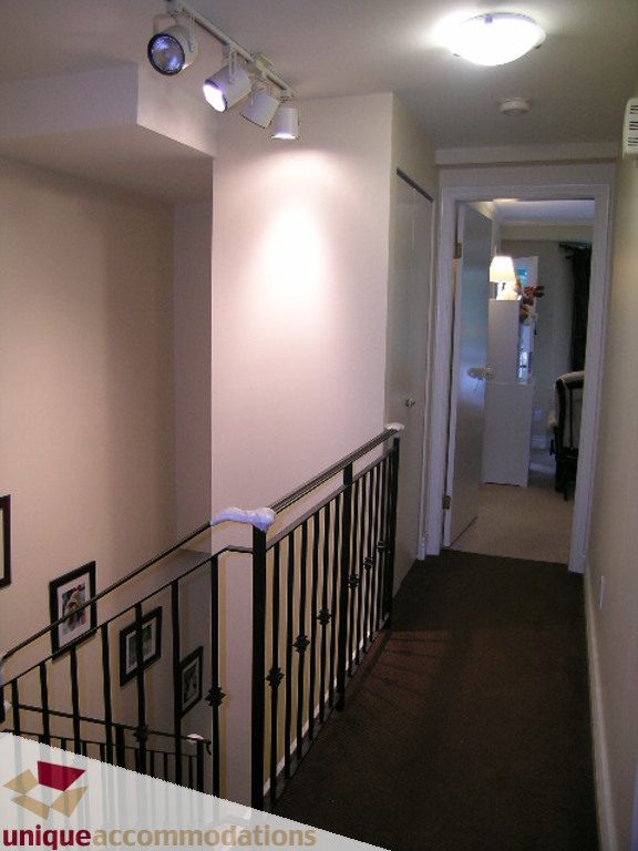 Foyer with black metal railing and white walls, leading to a hallway with carpeted floors. - T15 - 1501 Howe Street, Vancouver Downtown