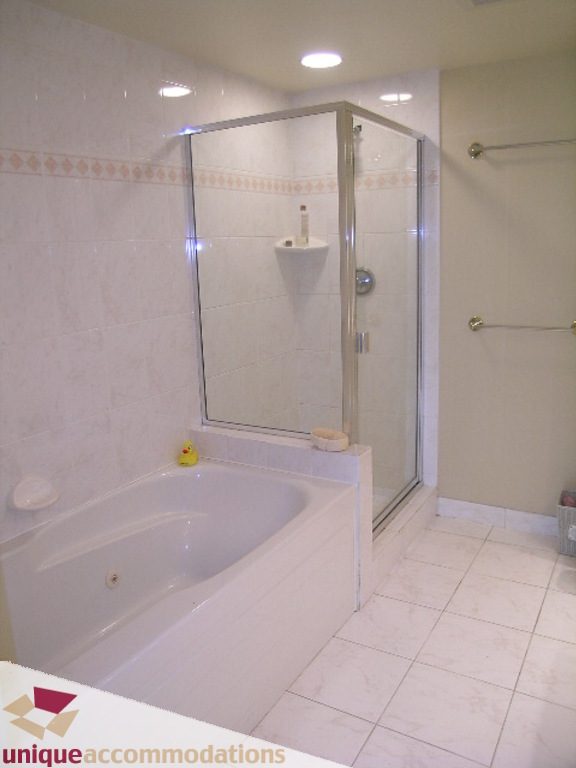 Furnished bathroom with glass shower and bathtub, white tiles, and grab bars. - T15 - 1501 Howe Street, Vancouver Downtown